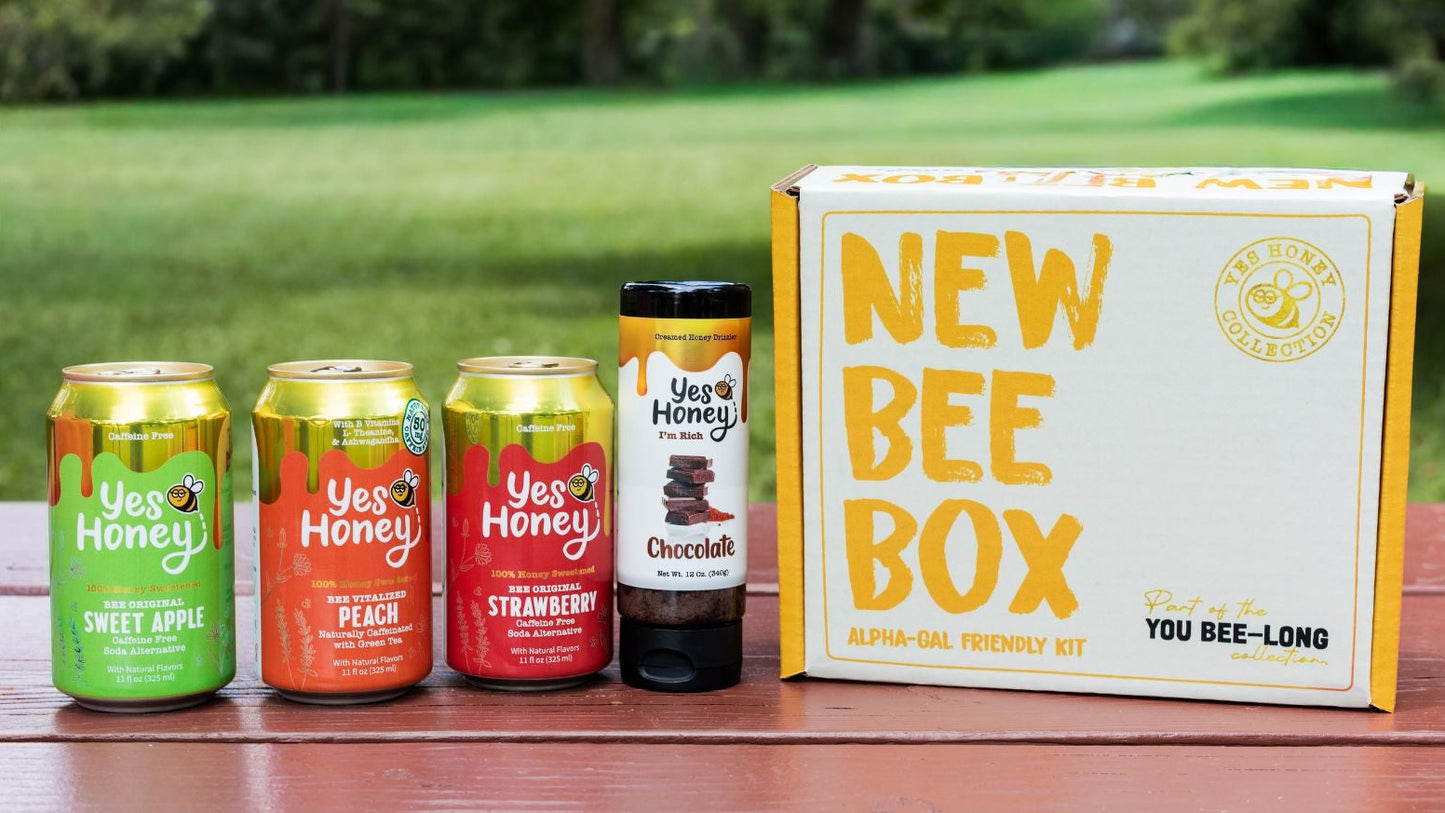 An Alpha Gal Friendly  gift set from Yes Honey displayed on an outdoor wooden table with 3 honey sweetened sodas and a chocolate honey drizzler.